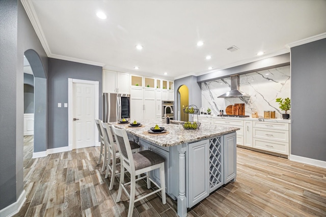 kitchen with a center island with sink, white cabinets, island exhaust hood, and appliances with stainless steel finishes