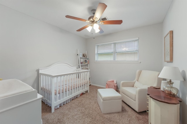 carpeted bedroom with ceiling fan and a crib