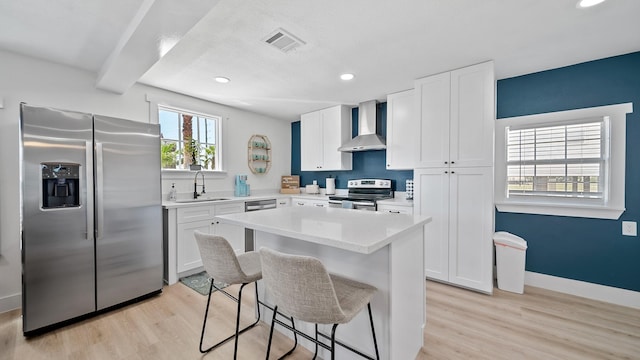 kitchen featuring white cabinetry, appliances with stainless steel finishes, wall chimney exhaust hood, sink, and light hardwood / wood-style flooring