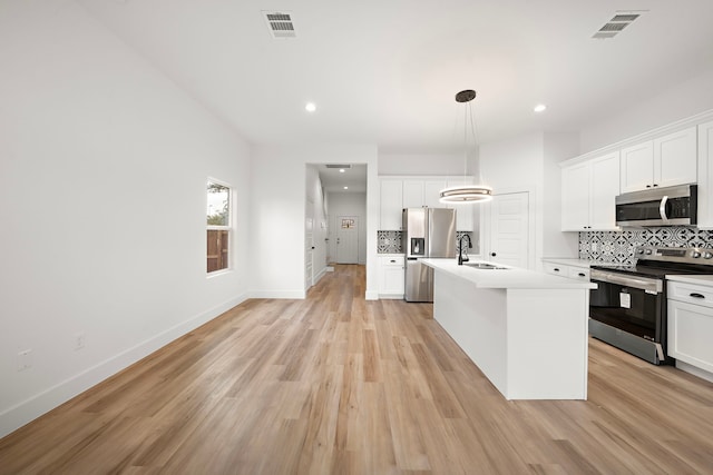 kitchen featuring decorative light fixtures, stainless steel appliances, a kitchen island with sink, and backsplash