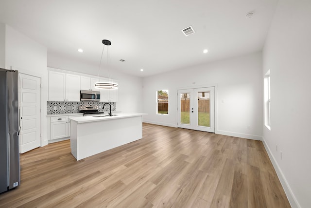 kitchen with decorative light fixtures, a center island with sink, tasteful backsplash, white cabinets, and appliances with stainless steel finishes