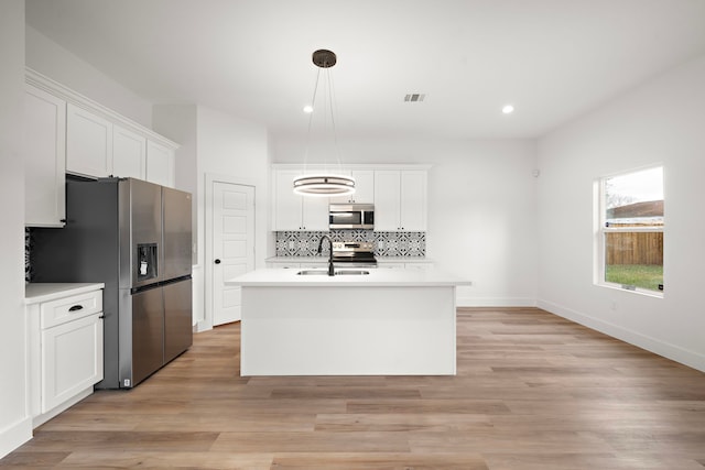 kitchen with stainless steel appliances, decorative light fixtures, white cabinetry, and a kitchen island with sink