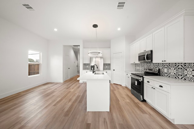 kitchen with a center island with sink, stainless steel appliances, pendant lighting, sink, and white cabinetry