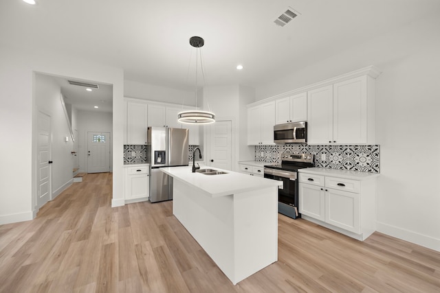 kitchen with stainless steel appliances, decorative light fixtures, white cabinetry, light hardwood / wood-style flooring, and a kitchen island with sink