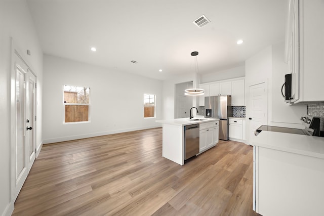 kitchen featuring hanging light fixtures, an island with sink, tasteful backsplash, white cabinets, and appliances with stainless steel finishes