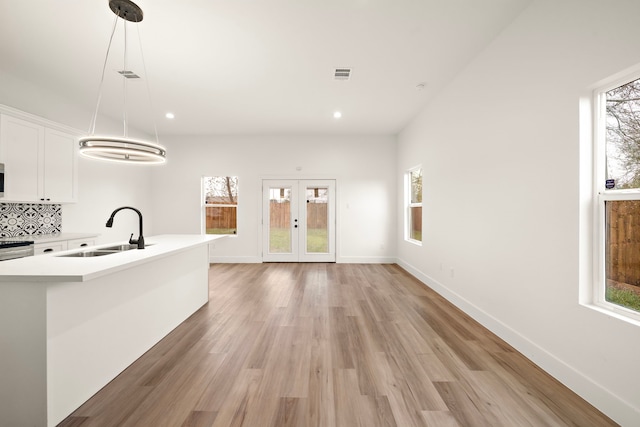 kitchen featuring light hardwood / wood-style flooring, pendant lighting, backsplash, white cabinetry, and sink