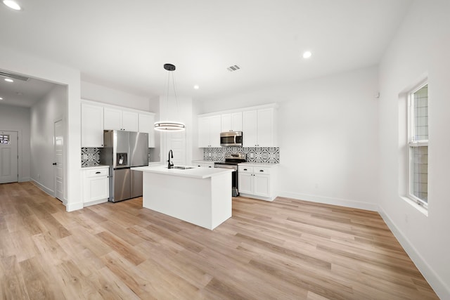 kitchen featuring appliances with stainless steel finishes, an island with sink, sink, white cabinetry, and decorative light fixtures