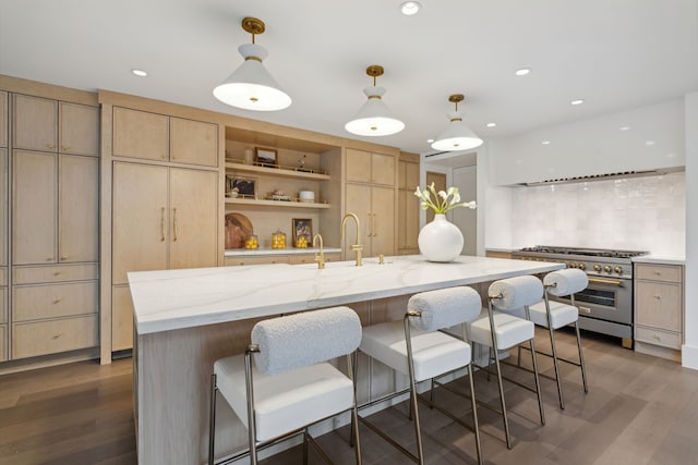 kitchen featuring light stone counters, pendant lighting, high end stainless steel range oven, an island with sink, and light brown cabinets