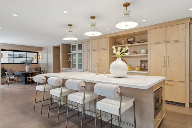 kitchen featuring a large island with sink, decorative light fixtures, built in microwave, and light brown cabinets