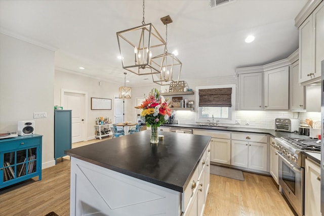 kitchen featuring decorative light fixtures, light hardwood / wood-style floors, decorative backsplash, stainless steel range, and sink