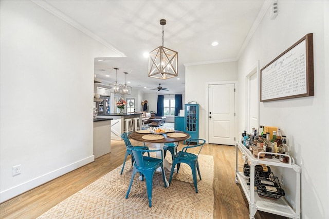 dining area with ceiling fan with notable chandelier, ornamental molding, and light hardwood / wood-style floors