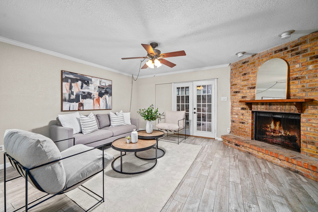 living room featuring hardwood / wood-style flooring, french doors, a brick fireplace, crown molding, and ceiling fan