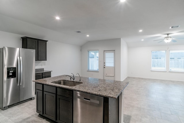 kitchen featuring light stone countertops, vaulted ceiling, stainless steel appliances, an island with sink, and sink