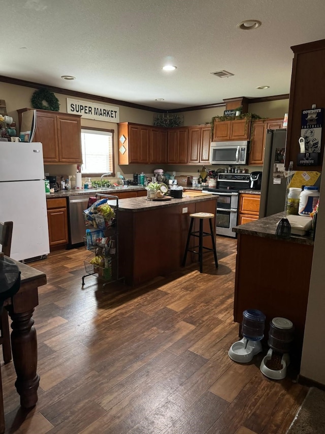 kitchen with a kitchen breakfast bar, stainless steel appliances, ornamental molding, dark hardwood / wood-style flooring, and a kitchen island