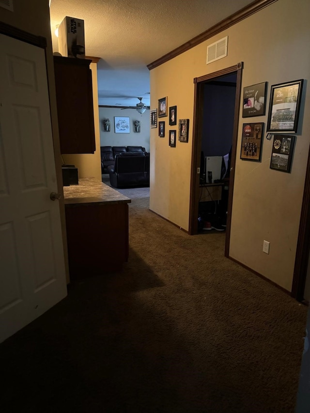 hall with ornamental molding, a textured ceiling, and dark carpet