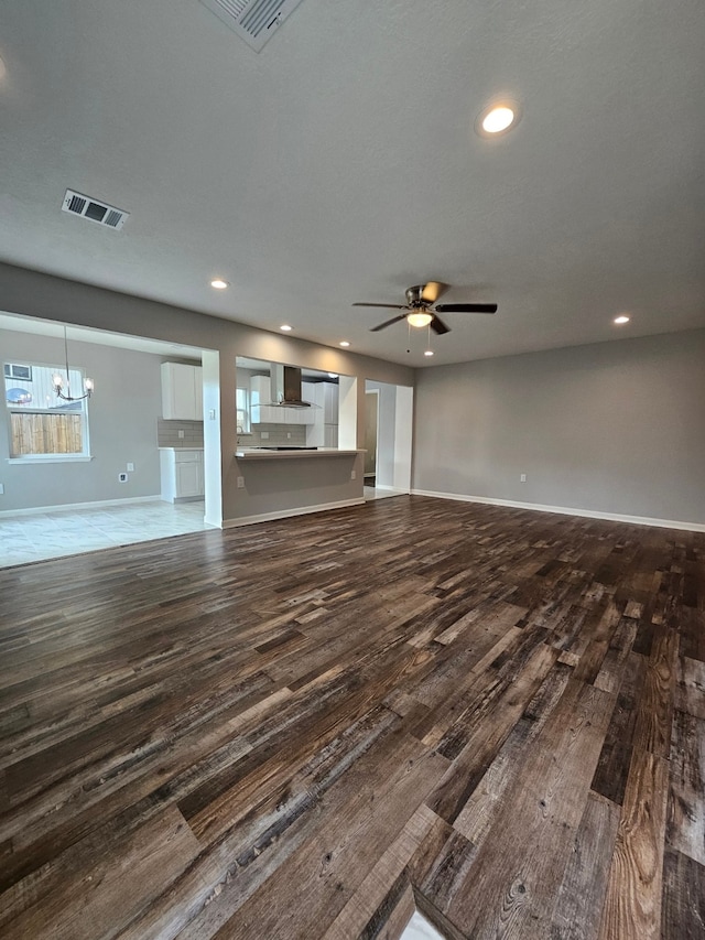 unfurnished living room with ceiling fan with notable chandelier and hardwood / wood-style flooring