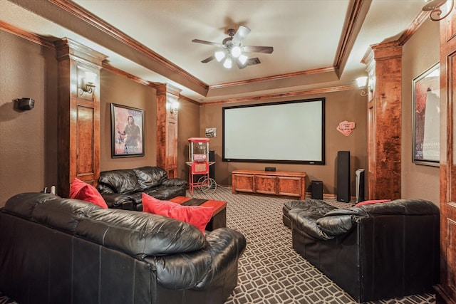 cinema room with decorative columns, a raised ceiling, ceiling fan, carpet floors, and crown molding