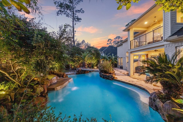 pool at dusk with a patio and ceiling fan