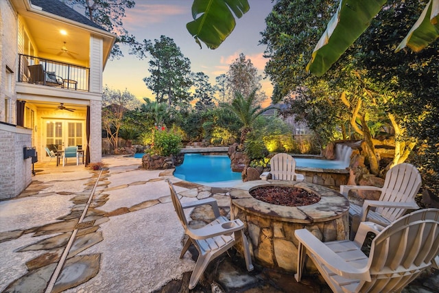 patio terrace at dusk with a balcony, ceiling fan, and an outdoor fire pit