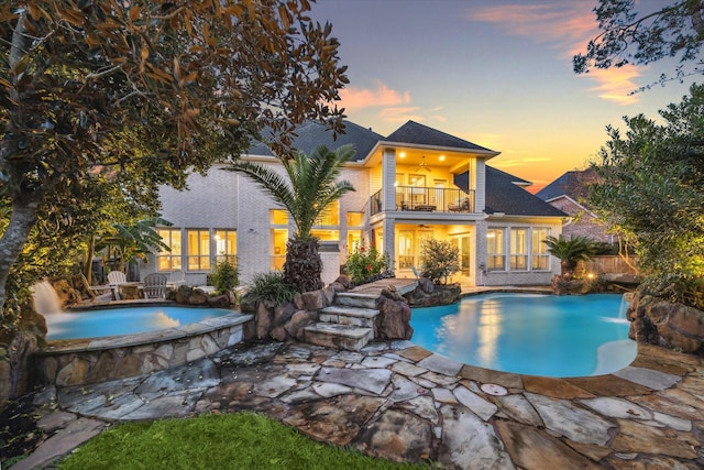 pool at dusk featuring ceiling fan, a patio, pool water feature, and an in ground hot tub