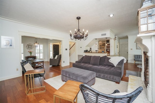 living room with wood-type flooring, a brick fireplace, an inviting chandelier, and crown molding