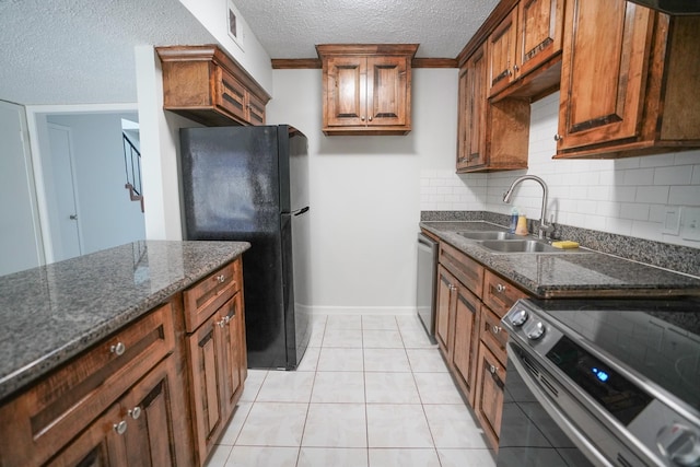 kitchen with sink, a textured ceiling, light tile patterned flooring, dark stone countertops, and appliances with stainless steel finishes