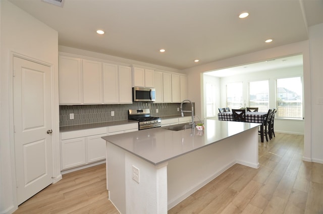 kitchen featuring a center island with sink, light hardwood / wood-style floors, white cabinetry, appliances with stainless steel finishes, and sink