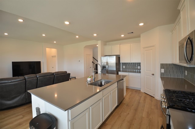 kitchen featuring stainless steel appliances, a center island with sink, decorative backsplash, white cabinets, and sink