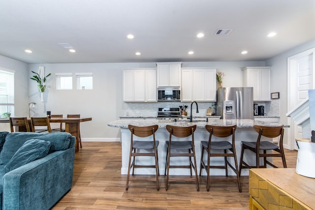 kitchen featuring stainless steel appliances, a center island with sink, light stone countertops, and white cabinetry