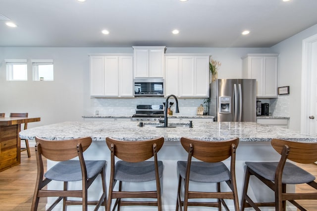 kitchen featuring stainless steel appliances, white cabinetry, a kitchen bar, and a center island with sink