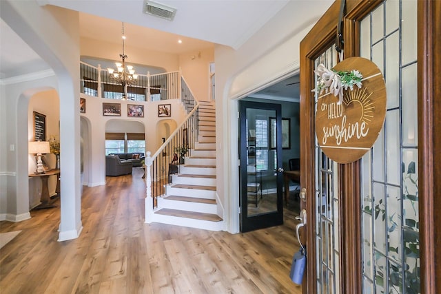 foyer entrance featuring crown molding, visible vents, wood finished floors, a chandelier, and stairs