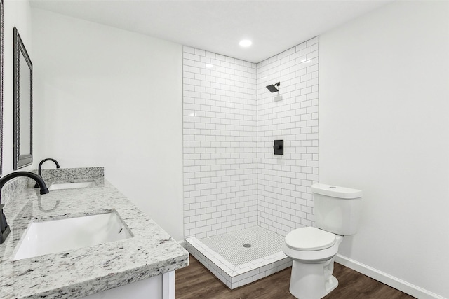 bathroom featuring wood-type flooring, tiled shower, vanity, and toilet