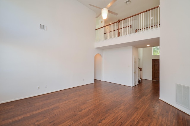 unfurnished living room featuring ceiling fan, dark wood-type flooring, and a high ceiling