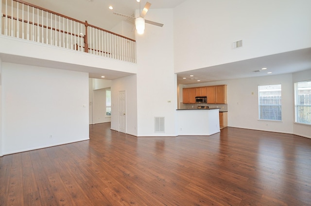 unfurnished living room featuring ceiling fan, a high ceiling, and dark hardwood / wood-style flooring