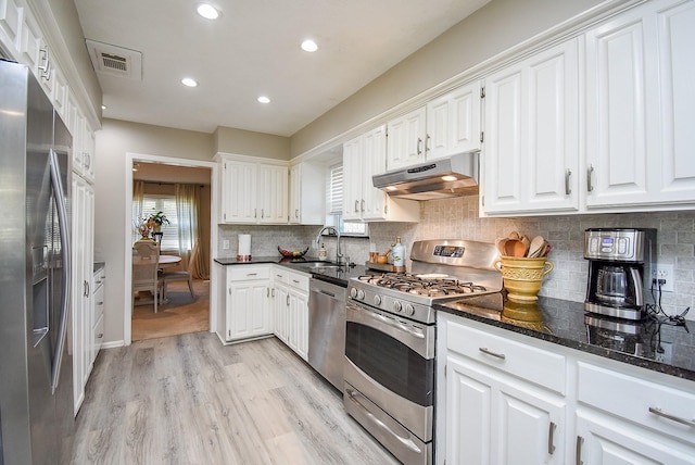 kitchen with sink, stainless steel appliances, dark stone counters, and white cabinetry