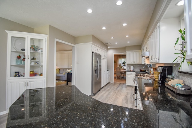 kitchen with stainless steel appliances, white cabinetry, dark stone countertops, and backsplash