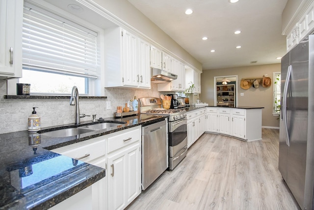 kitchen with appliances with stainless steel finishes, light wood-type flooring, dark stone counters, sink, and white cabinetry