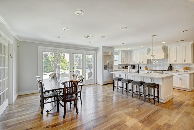 dining space with sink, ornamental molding, french doors, and light wood-type flooring