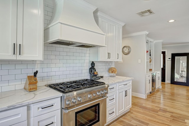 kitchen featuring high end stainless steel range oven, white cabinetry, custom exhaust hood, and decorative backsplash