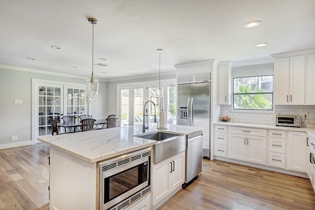 kitchen featuring decorative light fixtures, sink, built in appliances, white cabinetry, and an island with sink