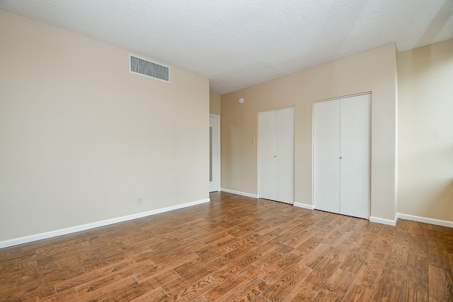 unfurnished bedroom featuring two closets, hardwood / wood-style floors, and a textured ceiling