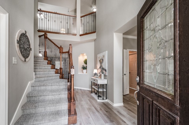 entryway with a high ceiling, ornamental molding, and light hardwood / wood-style floors