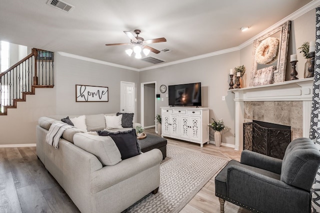 living room with light hardwood / wood-style floors, ceiling fan, a tile fireplace, and crown molding