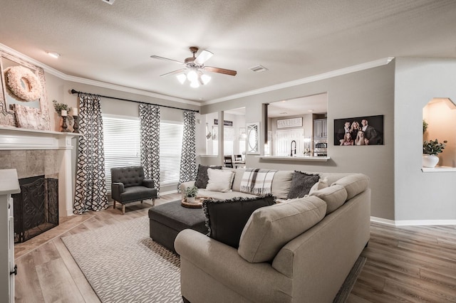 living room with a fireplace, light wood-type flooring, ceiling fan, and ornamental molding