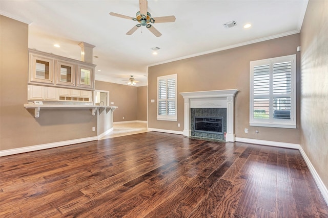 unfurnished living room featuring a high end fireplace, wood-type flooring, ceiling fan, and crown molding