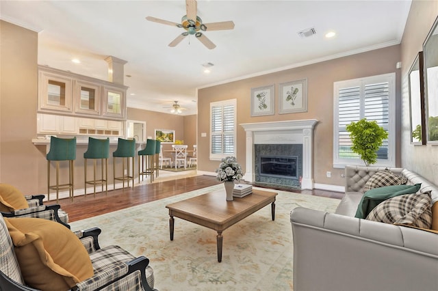 living room featuring crown molding, light hardwood / wood-style flooring, a high end fireplace, and ceiling fan