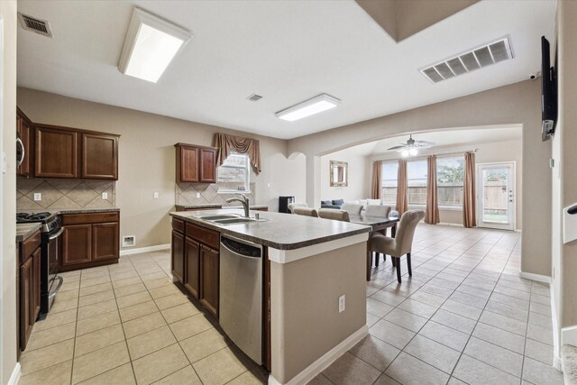 kitchen featuring dishwasher, a center island with sink, light tile patterned floors, sink, and gas range