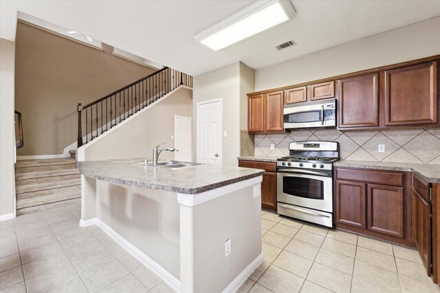 kitchen with stainless steel appliances, light tile patterned floors, decorative backsplash, a kitchen island with sink, and sink