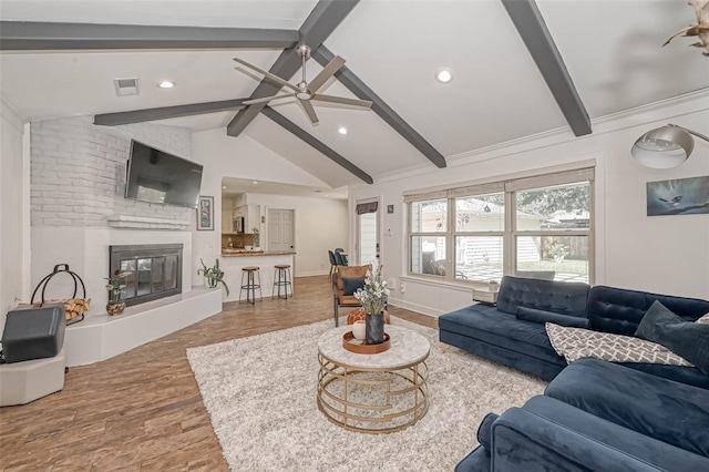 living room with wood-type flooring, a large fireplace, vaulted ceiling with beams, and ceiling fan