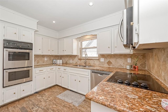 kitchen with light stone countertops, crown molding, white cabinetry, appliances with stainless steel finishes, and sink